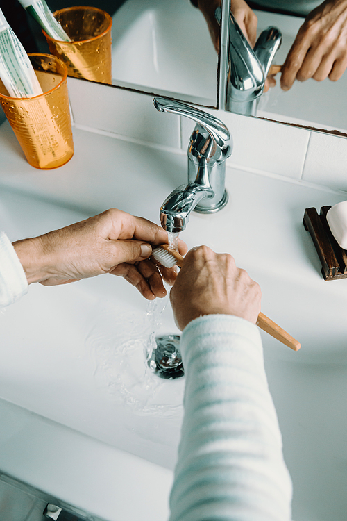 Old woman washes bamboo toothbrush with water and washes her teeth