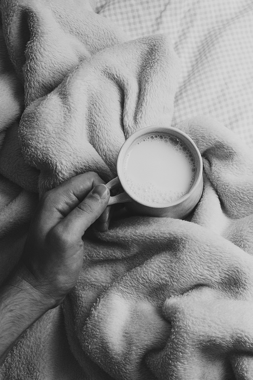 A cup of milk over a cozy blanket with a hand