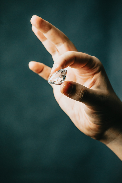 A hand grabbing a diamond with copy space over a dark background