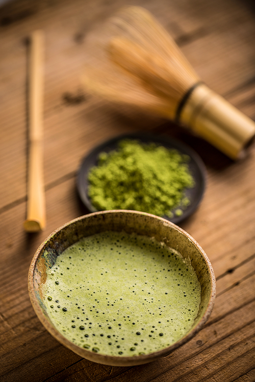 Organic green matcha tea in a bowl on wooden background