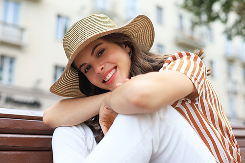 Beautiful smiling young brunette woman sitting on bench in park