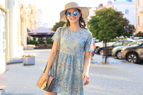 Portrait fashion woman in blue dress in sunglasses walking on street and holding smartphone in her hand