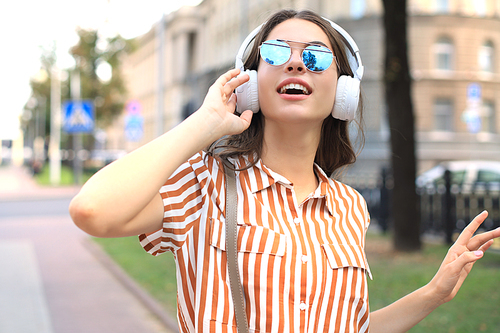 Smiling happy young beautiful woman in earphones walking outdoors in city