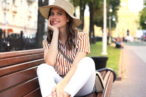 Beautiful smiling young brunette woman sitting on bench in park