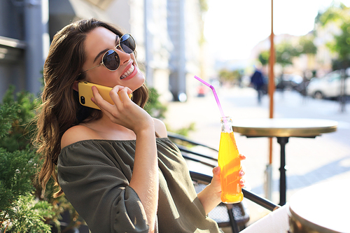 Attractive laughing woman talking on cellphone while sitting in cafe outdoors