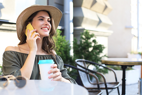 Attractive laughing woman talking on cellphone while sitting in cafe outdoors