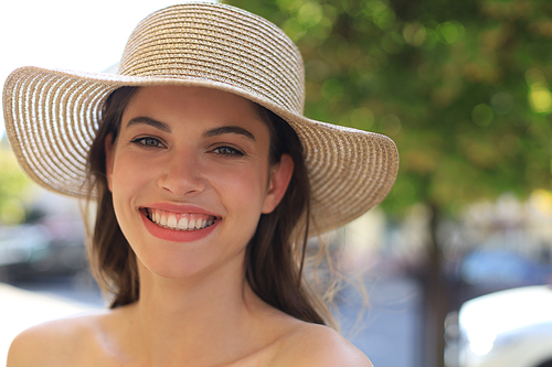 Photo of smiling young brunette woman in hat walking by street