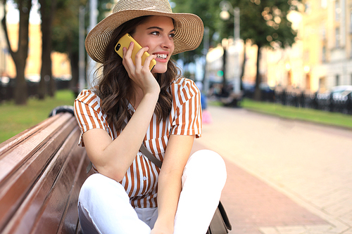 Attractive laughing woman talking on cellphone while sitting on bench outdoors.