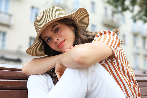 Beautiful smiling young brunette woman sitting on bench in park