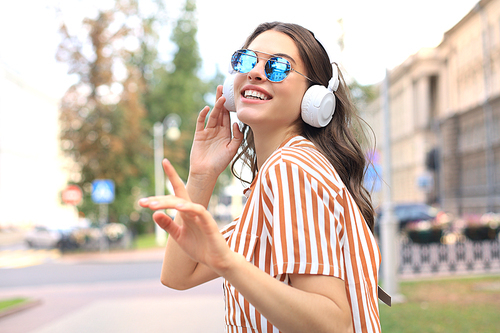 Smiling happy young beautiful woman in earphones walking outdoors in city