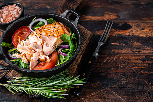 Grilled salmon fish fillet steak with fresh salad arugula, avocado and tomato in a pan. Dark wooden background. Top view. Copy space.