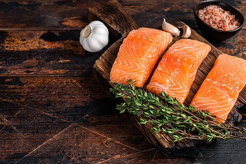 Fresh Raw salmon fish fillet steaks on wooden board with thyme. Dark wooden background. Top view. Copy space.