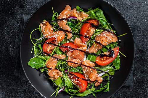 Salmon salad with fish slices, arugula, tomato and green vegetables. Black background. Top View.