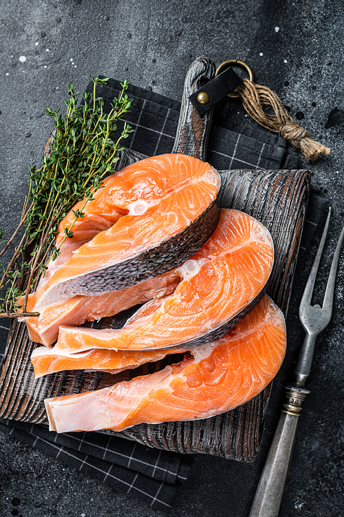 Raw Salmon or trout steaks, fish prepared for cooking on wooden board. Black background. Top view.