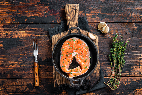 Trout or Salmon raw steaks in a pan with thyme. Dark wooden background. Top view.