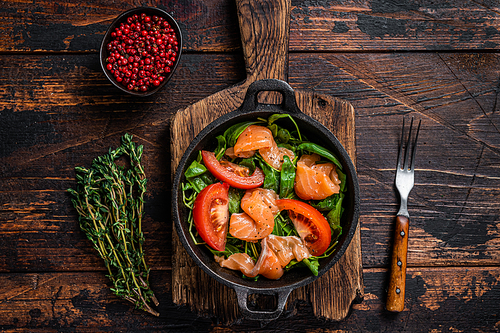 Fresh salmon salad with arugula, tomato and green vegetables. Dark wooden background. Top View.