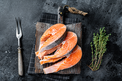Raw Salmon or trout steaks, fish prepared for cooking on wooden board. Black background. Top view.