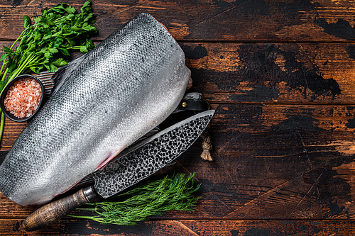 Big piece of Raw cut salmon fish on a wooden cutting board with chef knife. Dark Wooden background. Top view. Copy space.