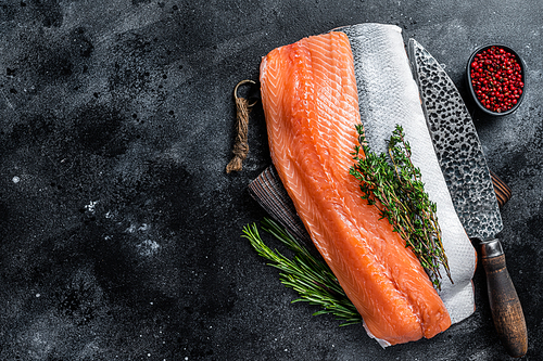 Fresh raw salmon fillet fish on cutting board with knife. Black background. Top view. Copy space.