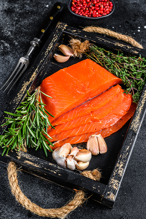 Smoked sliced salmon fillet in a wooden tray with herbs. Black background. Top view.