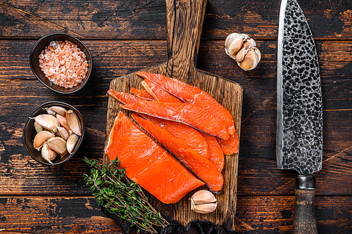 Sliced Smoked salmon fillet on a wooden cutting board with herbs. Dark wooden background. Top view.