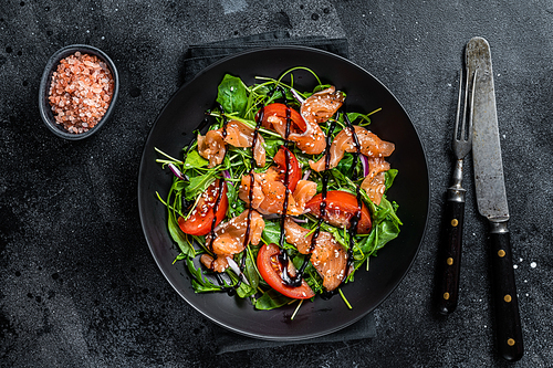 Salmon salad with fish slices, arugula, tomato and green vegetables. Black background. Top View.