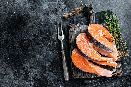 Raw Salmon or trout steaks, fish prepared for cooking on wooden board. Black background. Top view. Copy space.