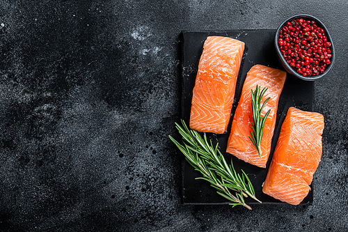 Raw salmon fillet steaks on marble board with herbs. Black background. Top view. Copy space.