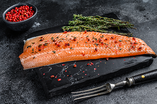 Salmon or trout sea fish fillet with salt and pink pepper. Black wooden background. Top view.