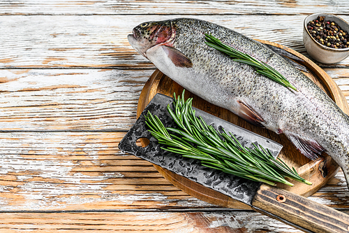 Rainbow trout on an wood board, with rosemary and cleaver. White wooden background. Top view. Copy space.