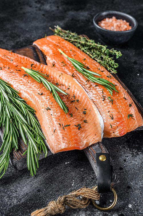 Salted salmon or trout sea fish fillet with spices and herbs. Black wooden background. Top view.