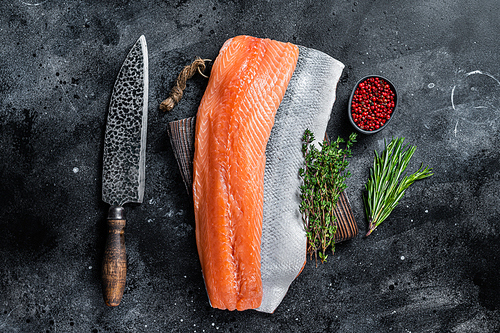 Fresh raw salmon fillet fish on cutting board with knife. Black background. Top view.