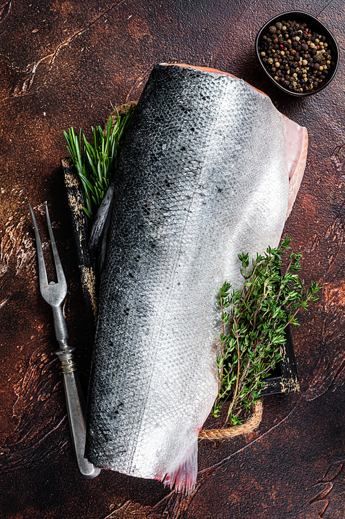 Slice of Raw cut salmon fish in a wooden tray with thyme. Dark background. Top view.