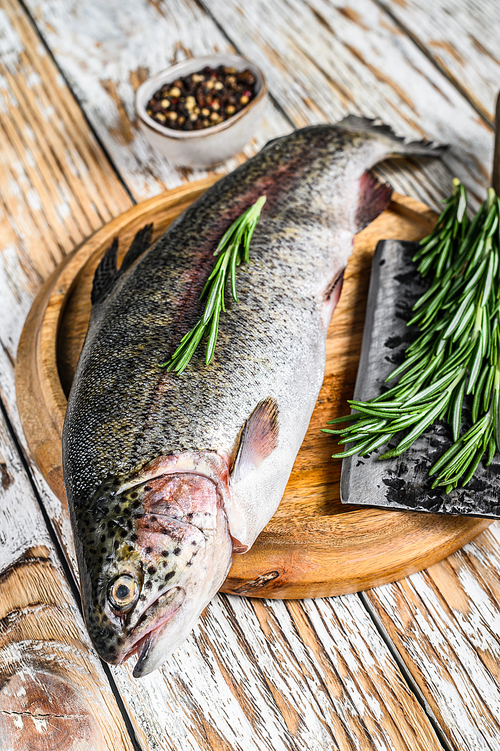 Rainbow trout on an wood board, with rosemary and cleaver. White wooden background. Top view.