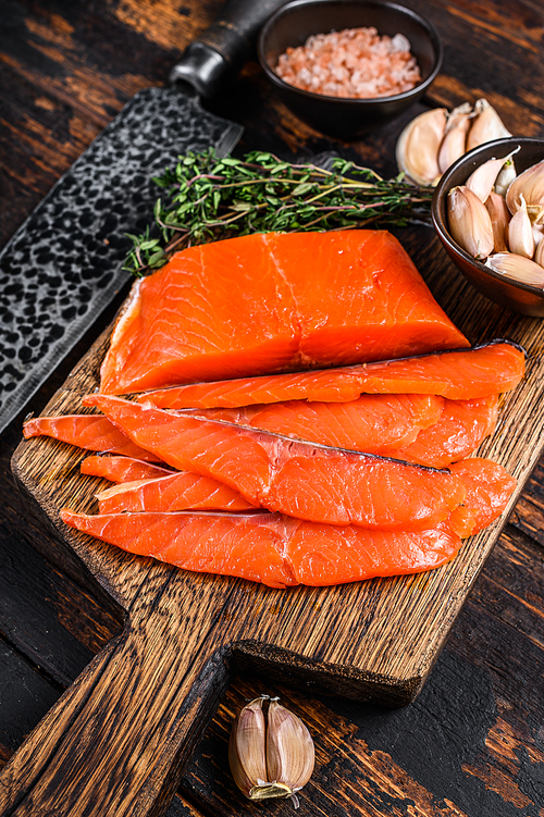 Sliced Smoked salmon fillet on a wooden cutting board with herbs. Dark wooden background. Top view.