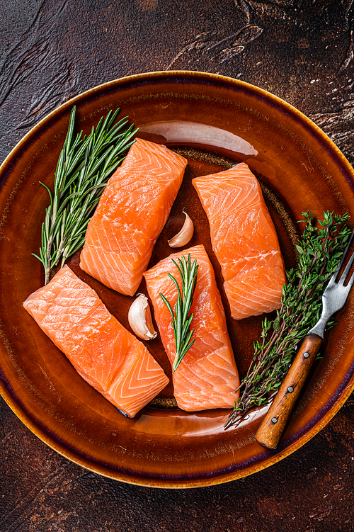 Fresh Raw salmon fish fillet steaks on rustic plate with thyme and rosemary. Dark background. Top view.