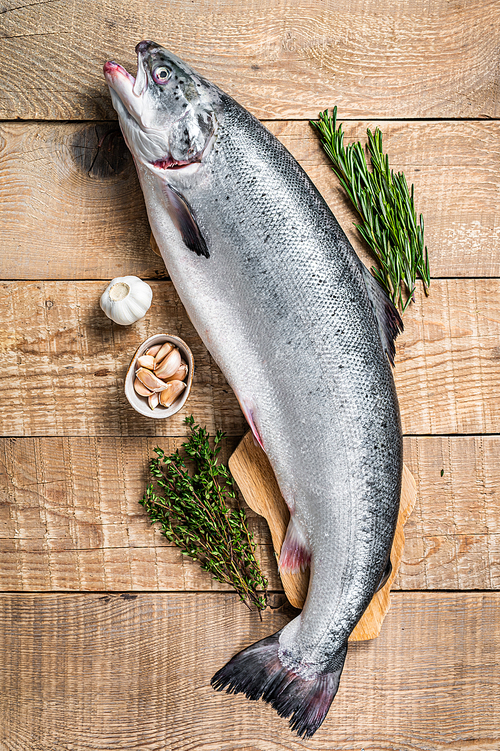 Raw marine salmon fish on a  wooden kichen table with herbs. Wooden background. Top view.