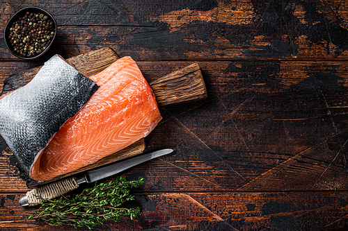 Salmon fillet fish on a  wooden board with herbs and salt. Dark wooden background. Top view. Copy space.