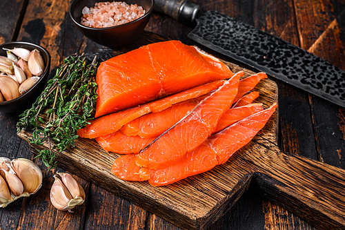 Sliced Smoked salmon fillet on a wooden cutting board with herbs. Dark wooden background. Top view.