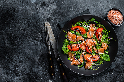 Salmon salad with fish slices, arugula, tomato and green vegetables. Black background. Top View. Copy space.