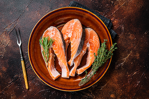 Salmon raw steaks on rustic plate with herbs. Dark background. Top view.