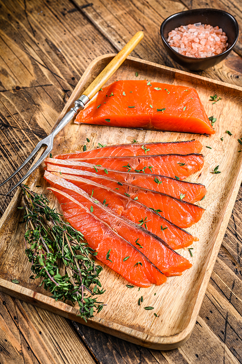 Salted salmon fillet slices in a wooden tray with thyme. wooden background. Top view.