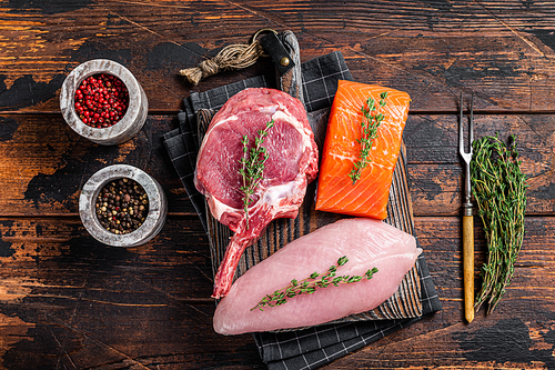 Raw steaks - fish salmon, beef meat and turkey breast fillet on a cutting board. Wooden background. Top view.