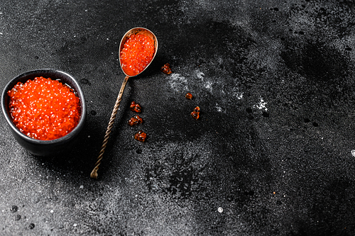 Salmon red caviar in an exquisite spoon. Black background. Top view. Copy space.