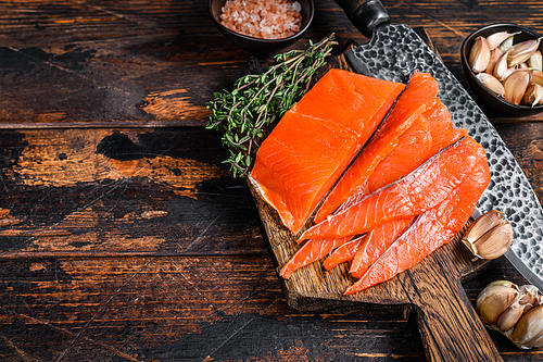 Sliced Smoked salmon fillet on a wooden cutting board with herbs. Dark wooden background. Top view. Copy space.