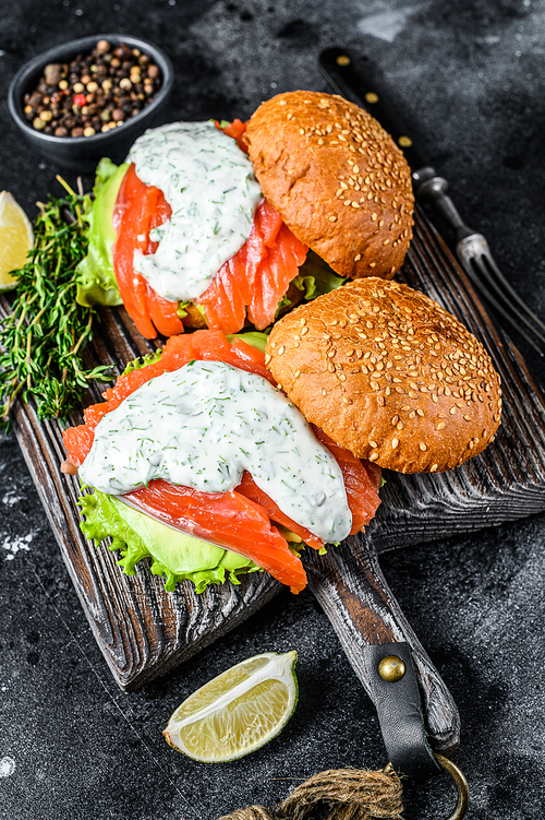 Fish burger with salted salmon, avocado, mustard sauce, cucumber and Iceberg salad. Black background. top view.