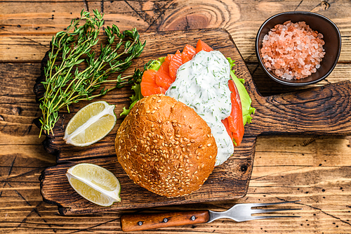 Sandwich with salted fish salmon, avocado, burger bun, mustard sauce and Iceberg salad. wooden background. top view.