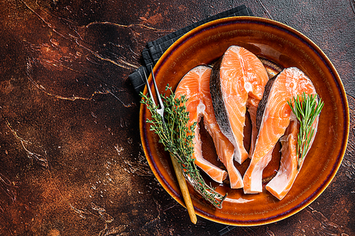 Salmon raw steaks on rustic plate with herbs. Dark background. Top view. Copy space.