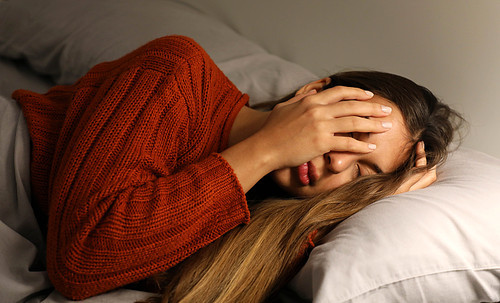 Young woman has a difficulty falling asleep. Girl with insomnia or headache cover her face with hand.