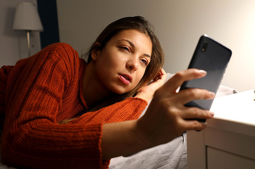 Girl suffering insomnia checks the time on the phone. Young woman awake late at night using smart phone lying in bed. Internet addiction, mobile abuse and insomnia concept.